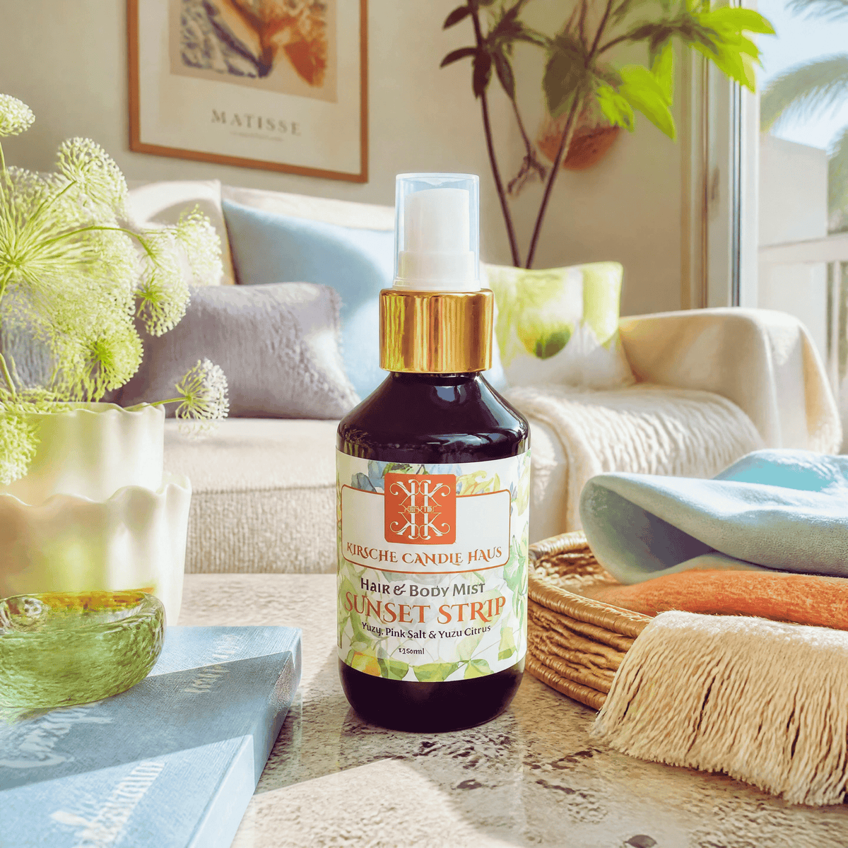 A bottle of Kirsche Candle Haus Sunset Strip hair & body mist sits on a table in a beautifully styled living room setting with a sofa, pillows, and plants in the background.Handpoured, vegan natural ingredients made in NZ.