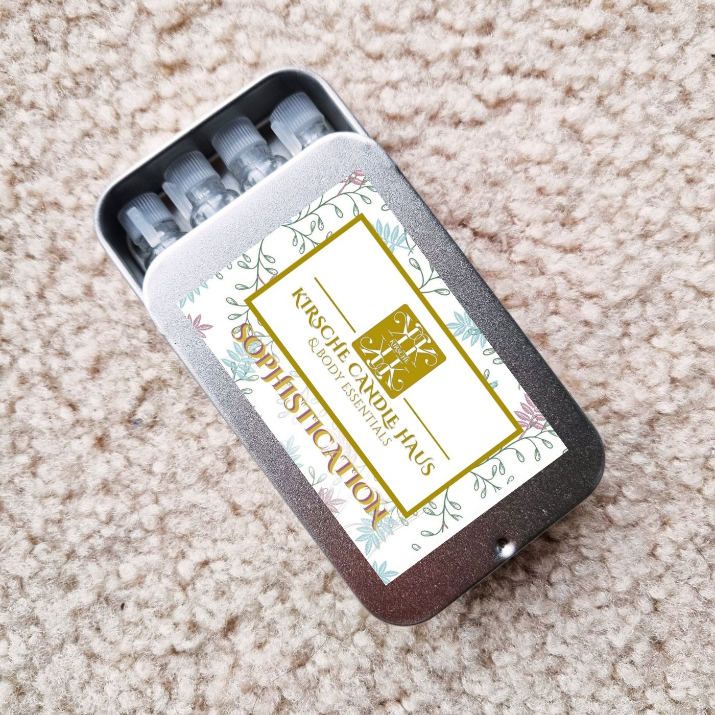 Set of small vials in a tin with a floral label and Kirsche Candle Haus logo; on a beige carpet